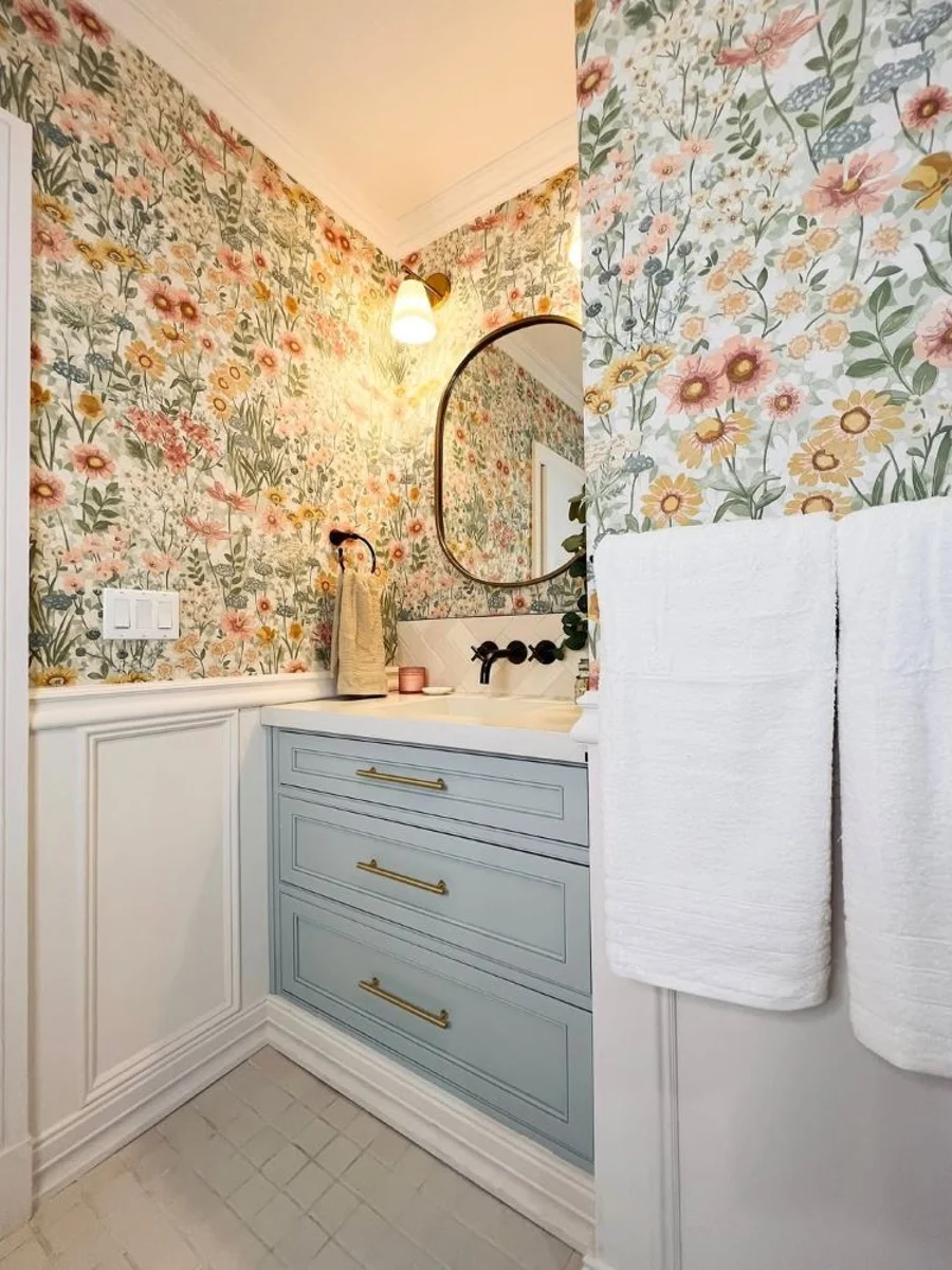 Wallflower Day wallpaper in a bathroom setting with blue cabinetry, white wall panelling and a circular mirror on the wall
