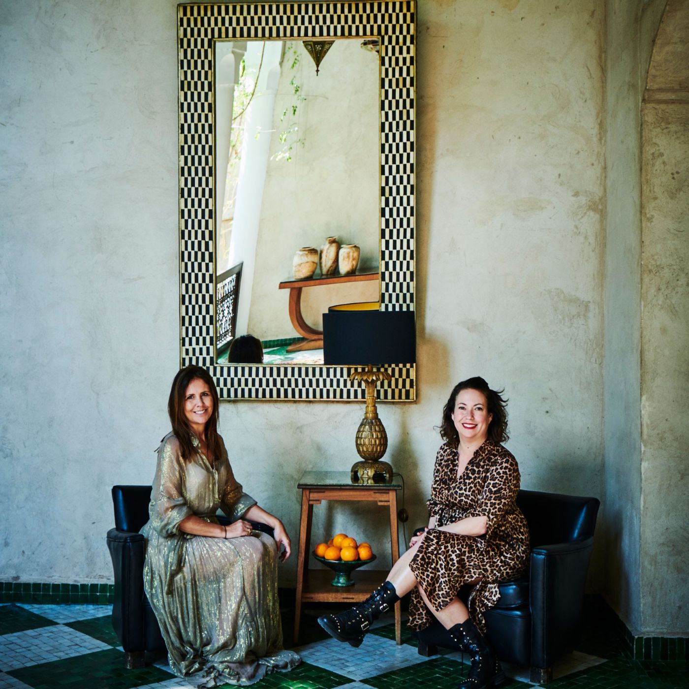 Image of Jane Rockett and Luct St George sat on chairs in front of a big mirror. Photography is by Catherine Gratwicke.