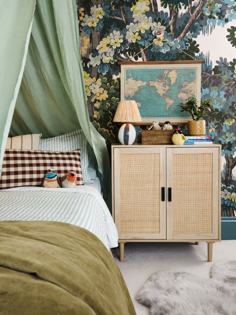 A children's bedroom featuring a lamp on a bedside cabinet and a picture of a map hanging on the wall, which is decorated with Bodenham Heritage Green Mural