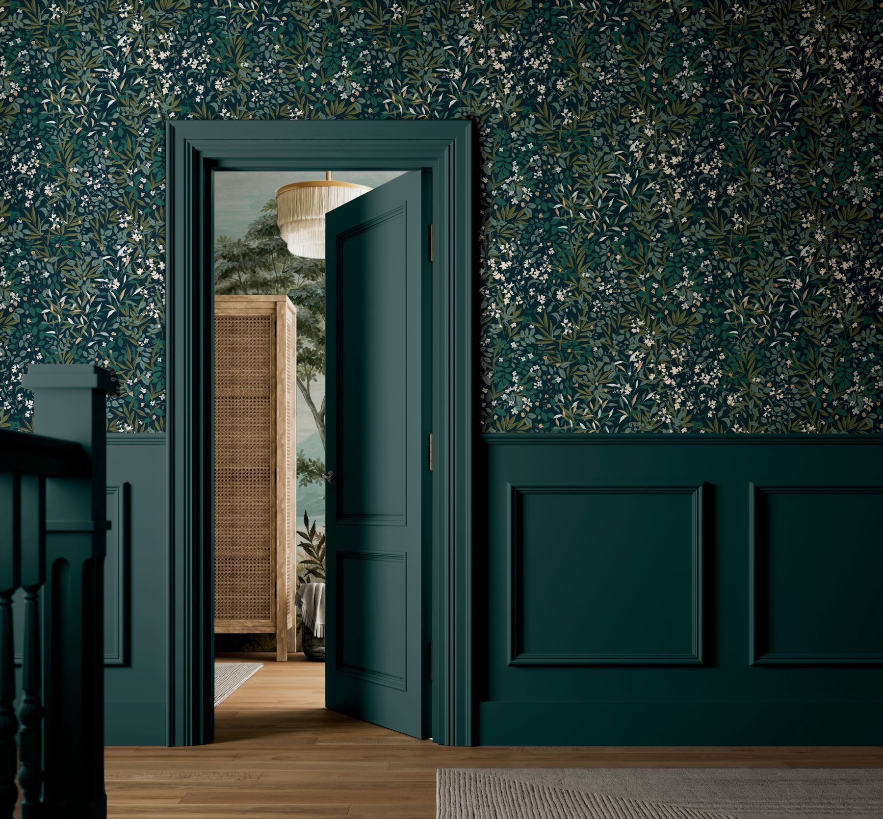 A hallway with dark teal panelled walls painted in Graham & Brown’s Petrol interior eggshell, paired with Reverie Navy wallpaper, leading into a room featuring a wicker screen, a fringed hanging light, and a tree‑patterned mural. A wooden floor and a light rug sit in the foreground.
