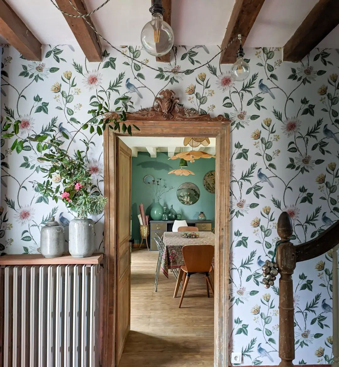 Nuit Lush wallpaper in a hallway setting, complemented by a floating shelf adorned with lush blooms. An open doorway leads seamlessly into the dining room, creating a beautifully connected, design‑led space.