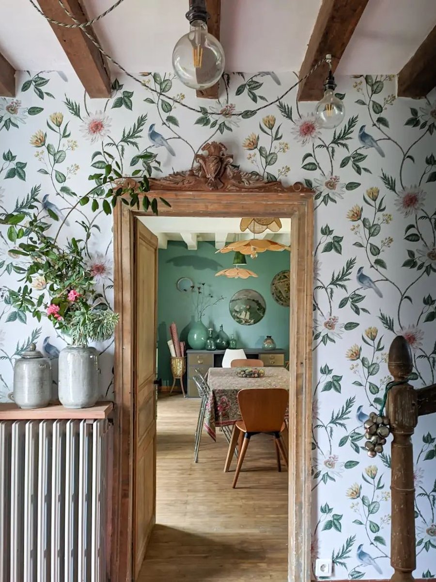 Nuit Lush wallpaper in a hallway setting, complemented by a floating shelf adorned with lush blooms. An open doorway leads seamlessly into the dining room, creating a beautifully connected, design‑led space.