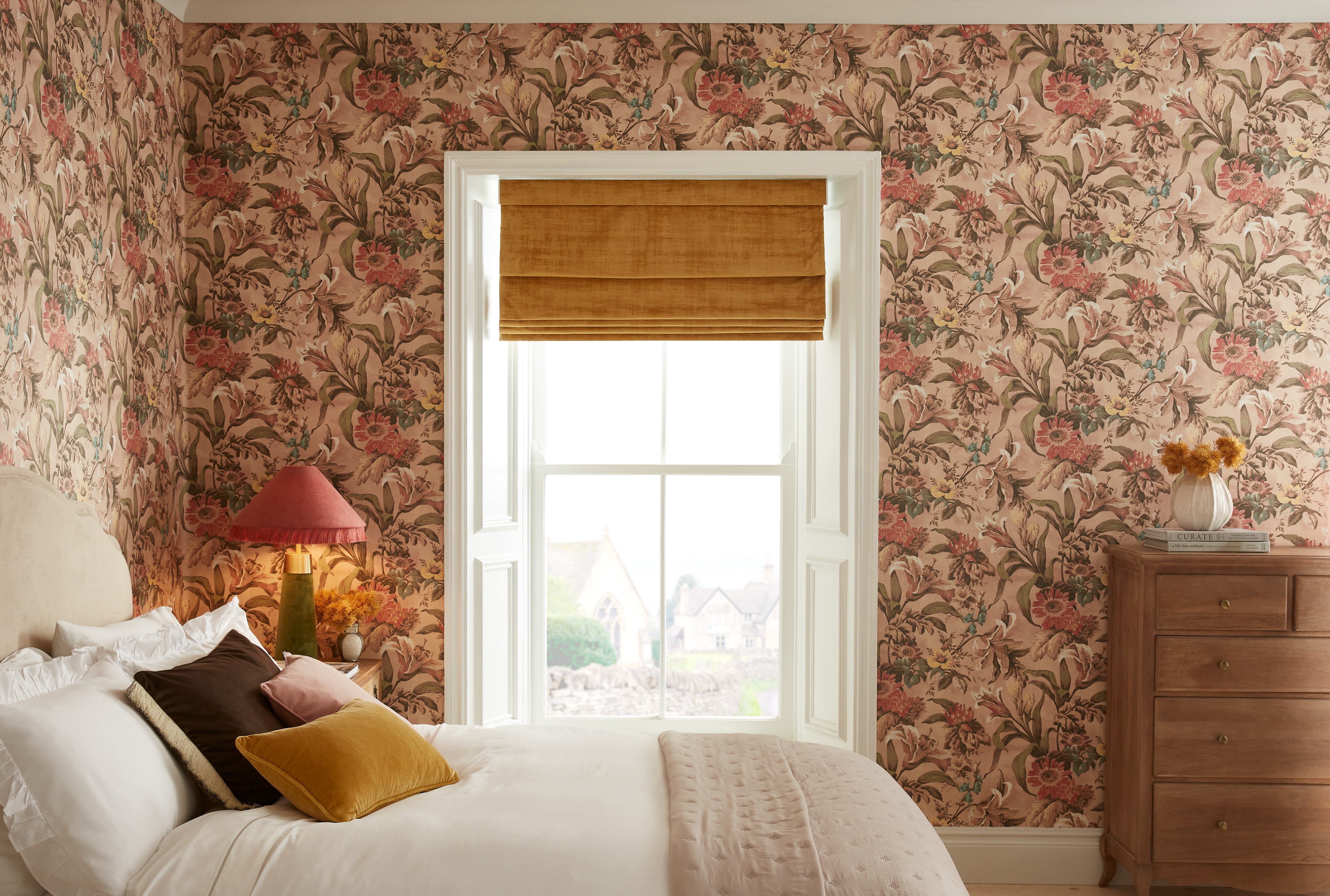 Elements Sunset roman blind partnered with Lys Whispering Rose wallpaper in a bedroom setting