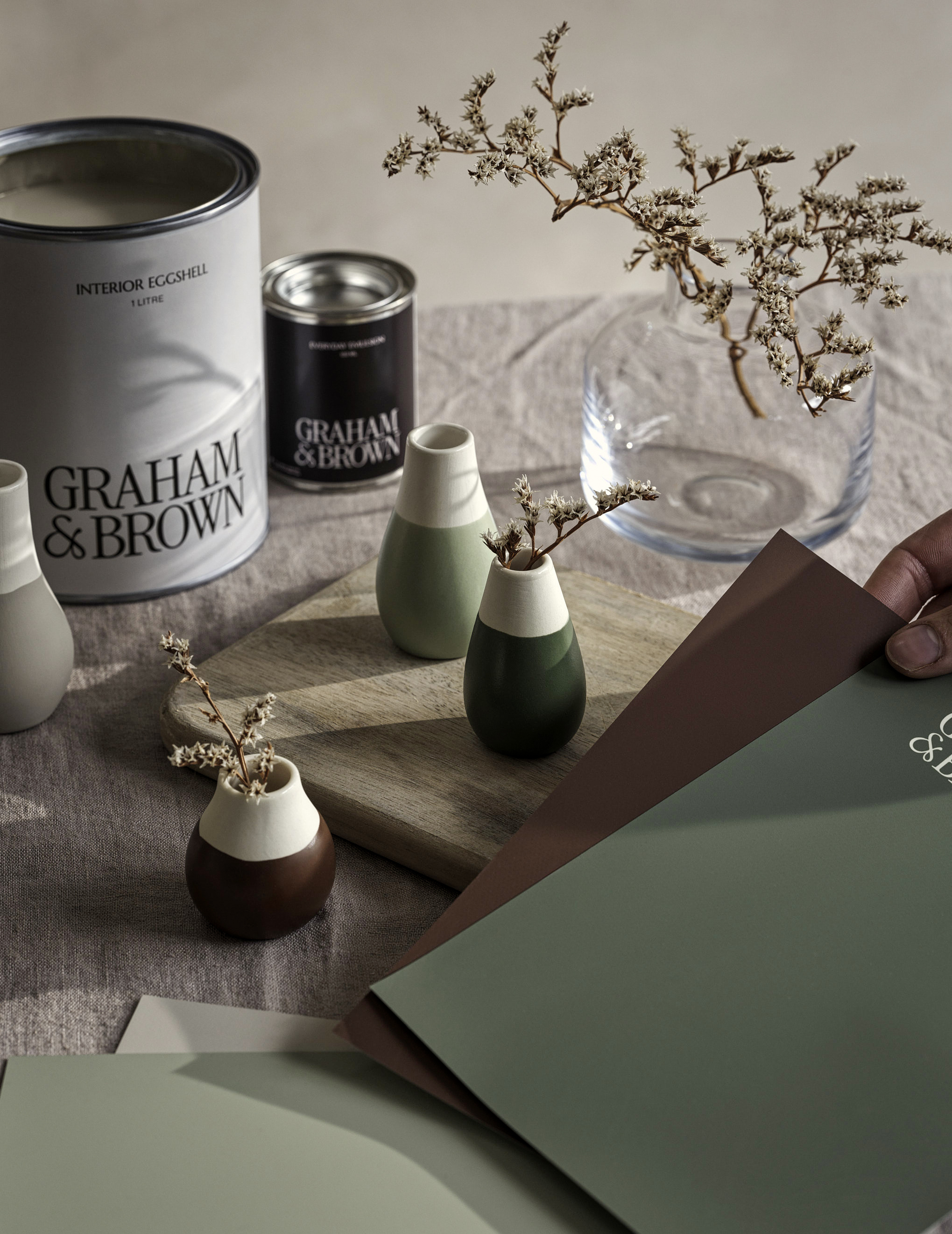 Moodboarding peel-and-stick paint samples on a dining room table with paint tins and decor in the background. 