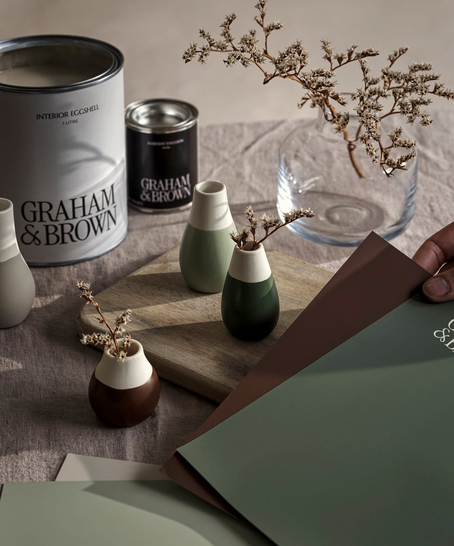 Moodboarding peel-and-stick paint samples on a dining room table with paint tins and decor in the background.