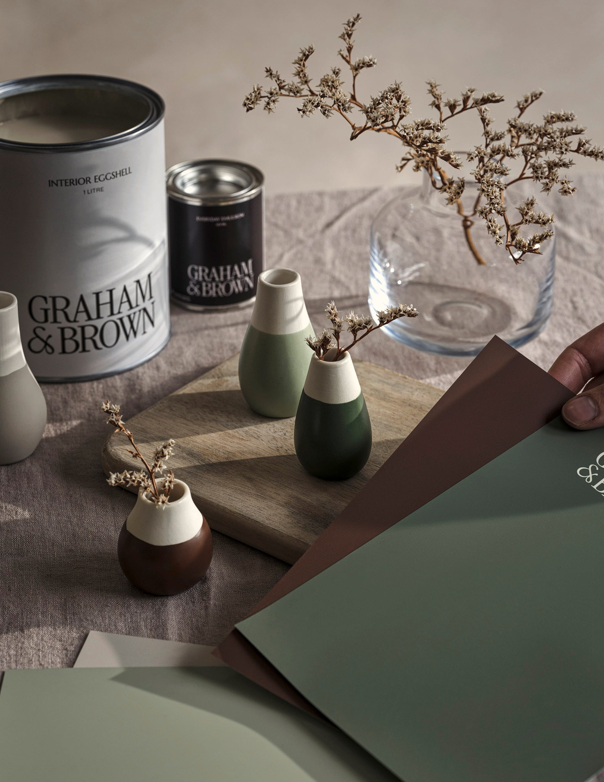 Moodboarding peel-and-stick paint samples on a dining room table with paint tins and decor in the background. 
