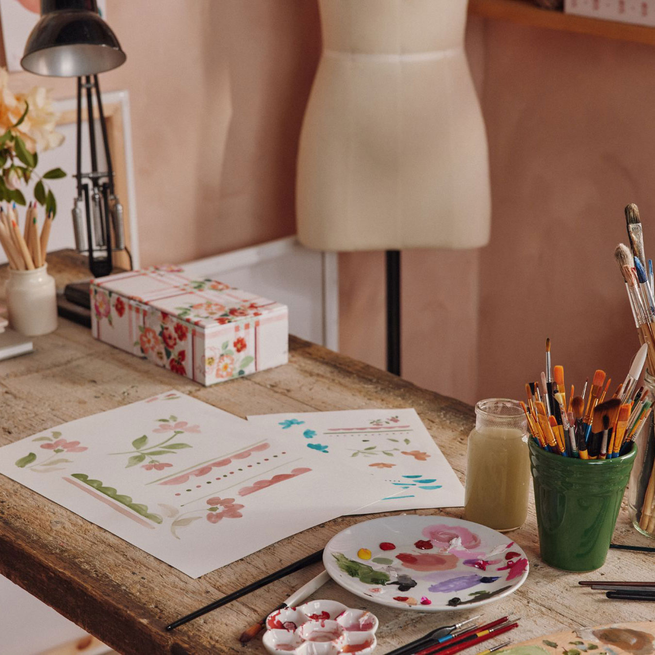 Cath Kidston wallpaper sketches on a desk with paintbrushes and pencils