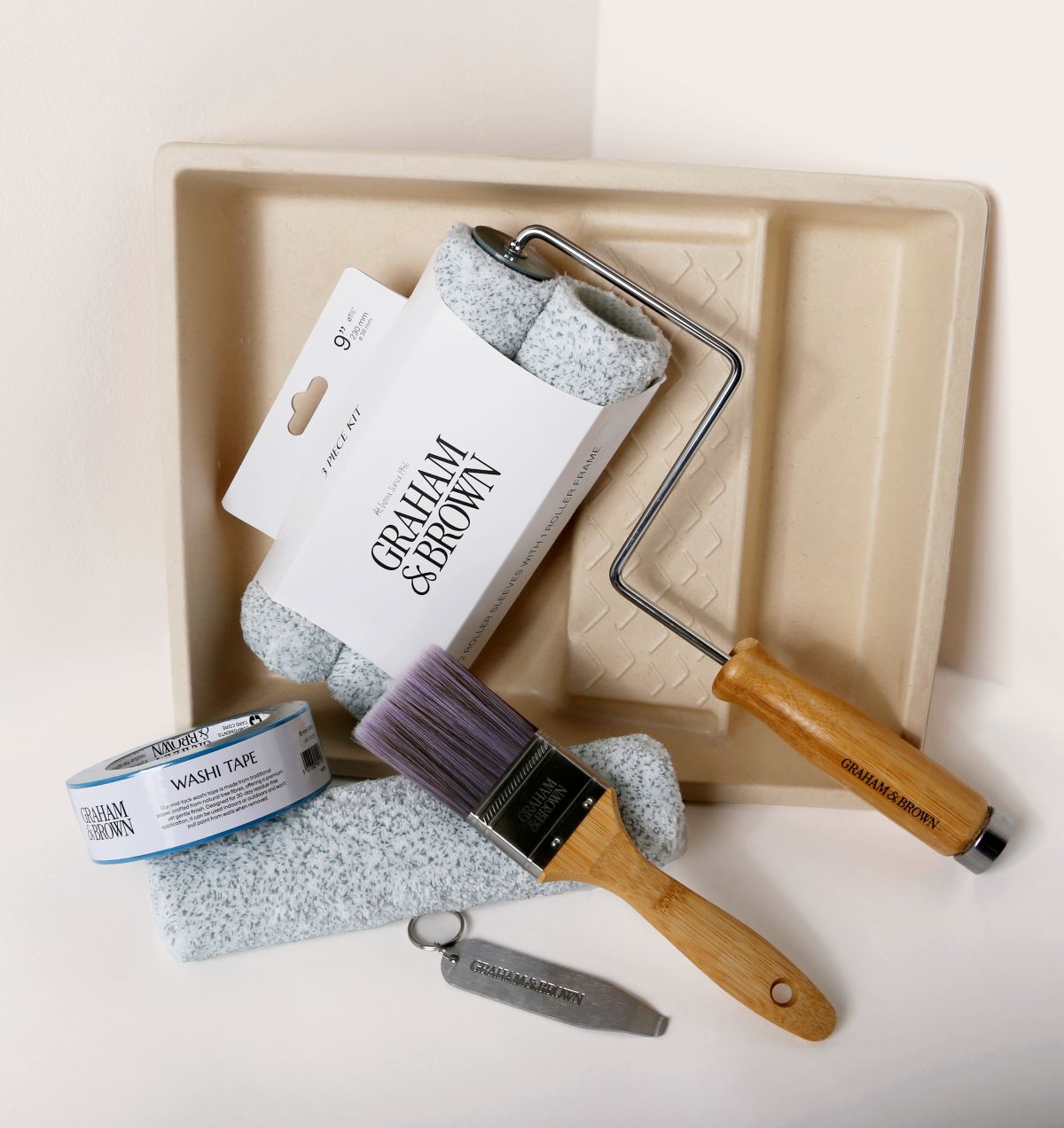 Paint kit contents arranged neatly, including brush, roller frame, roller sleeves, paint tray, can opener and washi tape.