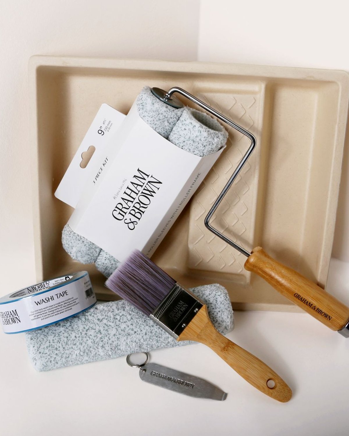 Paint kit contents arranged neatly, including brush, roller frame, roller sleeves, paint tray, can opener and washi tape.