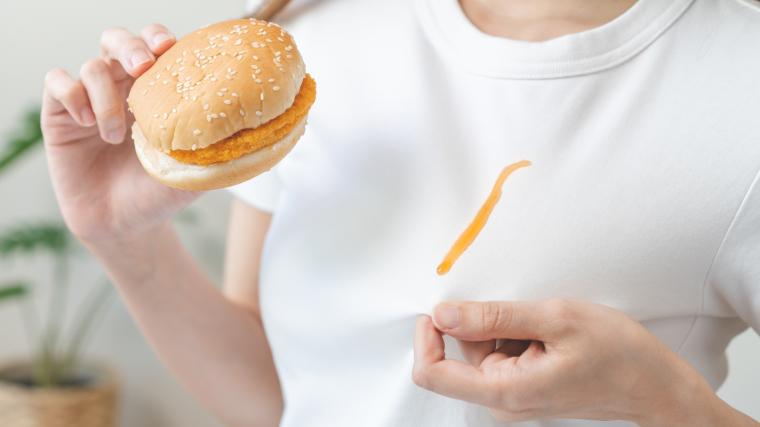 A person eating greasy food with a stain on clothes