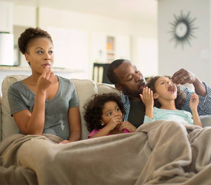 Mujer, hombre y dos niñas comen en sillón en casa