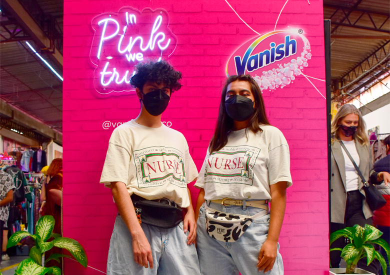 hombre y mujer vestidos con mismo outfit y cubrebocas negro frente a letrero rosa