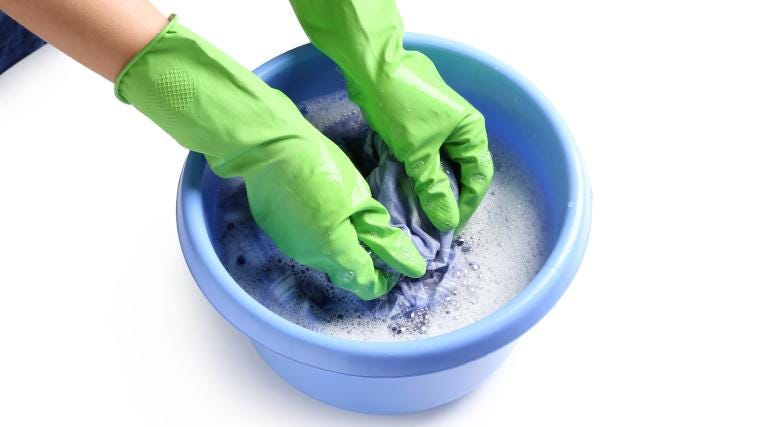 A person wearing gloves washing clothes in a tub of water