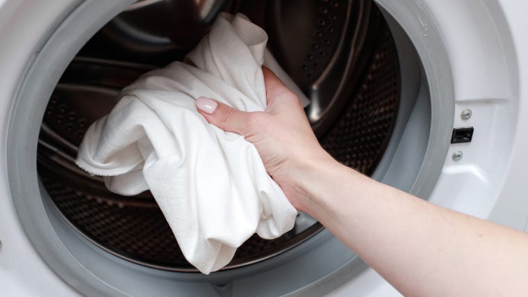 Person loading a washing machine with red stained clothes