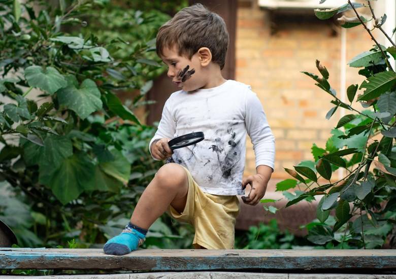 niño vestido de blanco con lupa y manchas de lodo