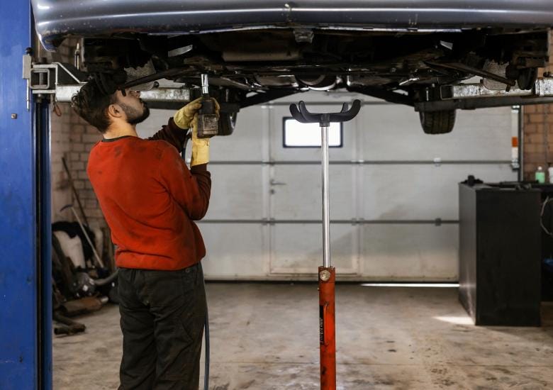 A person conducting maintaince checks a car with grease stains on shirt