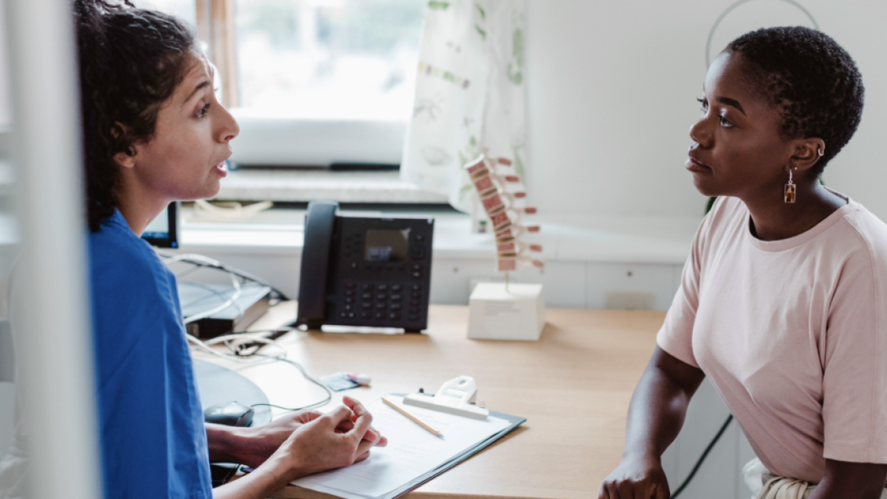 Image of a female healthcare professional sitting at a desk with a female patient 