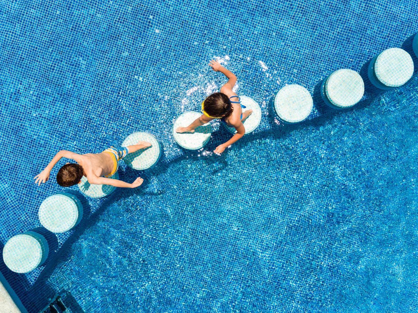 Kinder laufen über Trittsteine im Pool