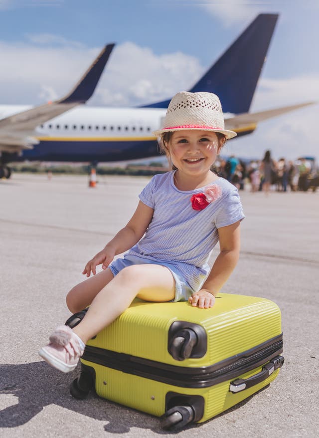 Fliegen mit Kleinkind und Baby Mädchen sitzt auf einem gelben Koffer vor einem Flugzeug