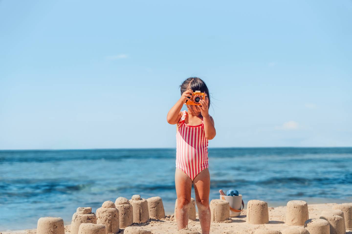 Mädchen fotografiert etwas und steht umgeben von Sandburgen am Meer