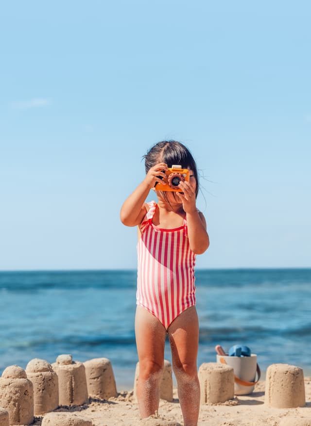 Alles Inclusive Mädchen fotografiert etwas und steht umgeben von Sandburgen am Meer
