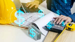 A construction worker with open plans while using a laptop and calculator A construction worker with open plans while using a laptop and calculator