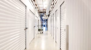 A bright, clean hallway inside a self-storage facility, lined with closed white metal doors on both sides. A bright, clean hallway inside a self-storage facility, lined with closed white metal doors on both sides.
