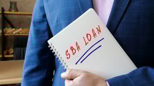 An image of a man in a suit holding a spiral notebook with the words SBA loan An image of a man in a suit holding a spiral notebook with the words SBA loan