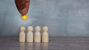 A hand holding a wood star above four wood block people A hand holding a wood star above four wood block people