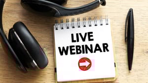 An image of the words live webinar on a spiral notebook with headphones nearby An image of the words live webinar on a spiral notebook with headphones nearby