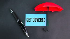 A pen and umbrella over a piece of blue paper with the words get covered on it A pen and umbrella over a piece of blue paper with the words get covered on it