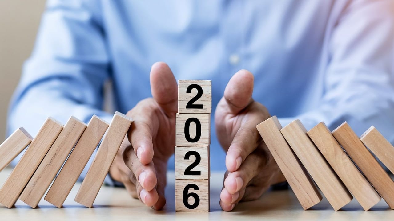 Hands stopping falling wooden blocks onto another block that says 2026 Hands stopping falling wooden blocks onto another block that says 2026
