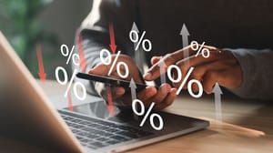 An image of a person with a cell phone and laptop with percentage signs hovering and up and down arrows in the background An image of a person with a cell phone and laptop with percentage signs hovering and up and down arrows in the background