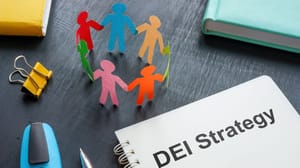 An image of colored paper people next to a notebook with the words DEI strategy An image of colored paper people next to a notebook with the words DEI strategy
