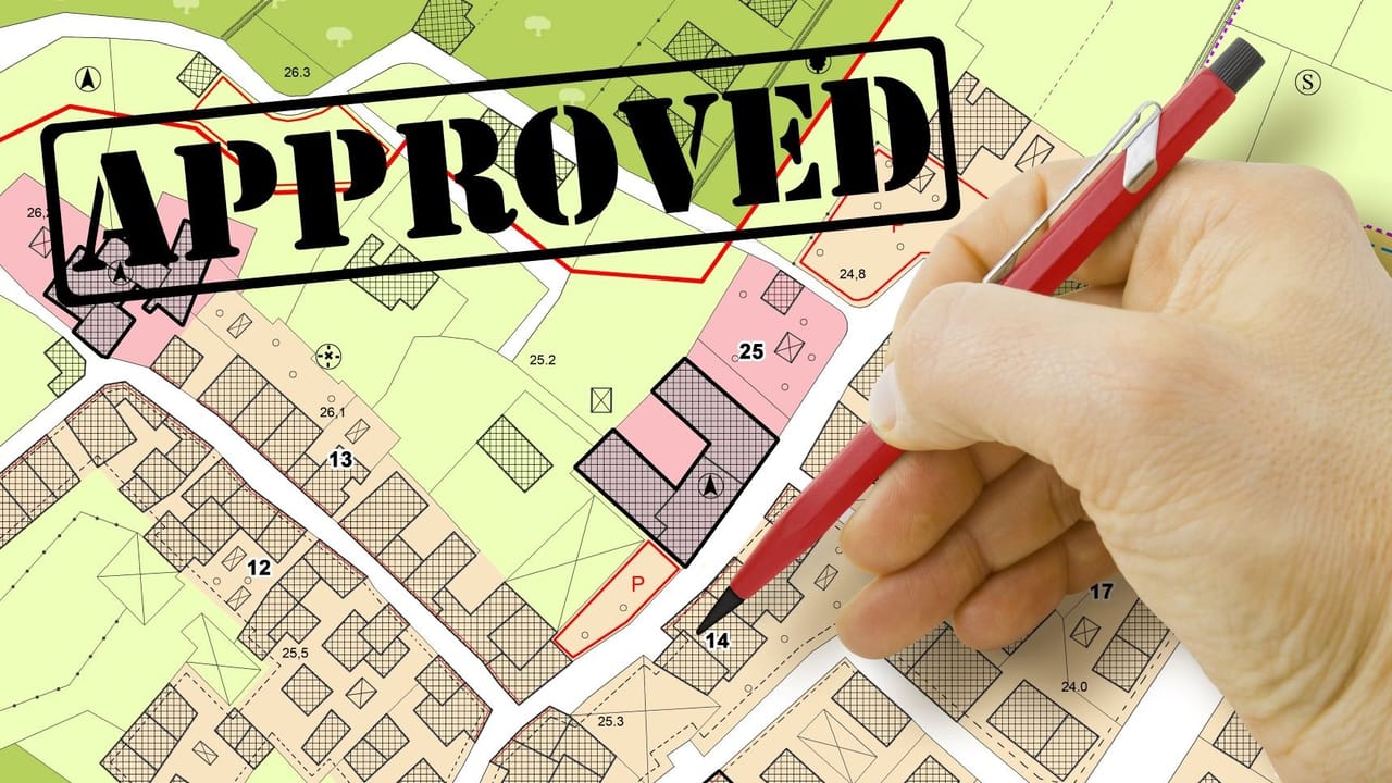 A colorful map of parcels with hand holding a pen marking one and the word approved above it A colorful map of parcels with hand holding a pen marking one and the word approved above it