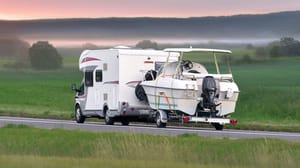 An RV pulling a trailered boat on a highway An RV pulling a trailered boat on a highway