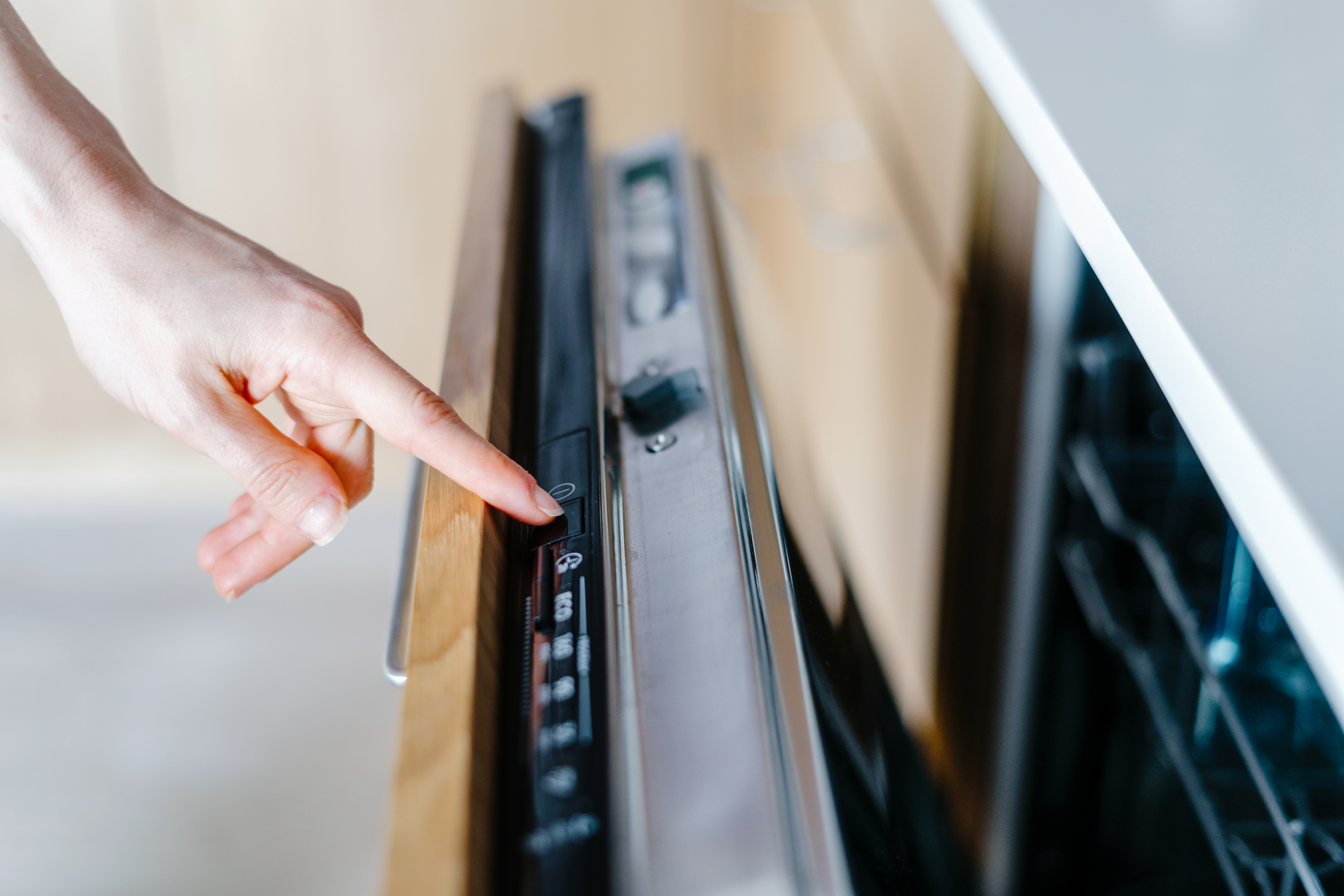 Gros plan montrant la main d’une femme qui appuie sur le bouton d’un lave-vaisselle moderne, prêt à commencer le cycle de nettoyage.