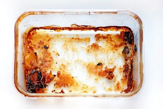 A glass casserole dish with caked-on tomato sauce.