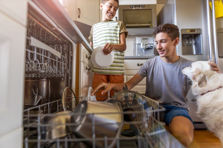 Deux enfants remplissent un lave-vaisselle dans une cuisine moderne.
