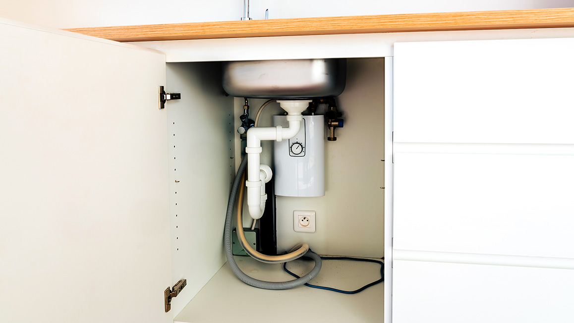 The underside of a sink with a drain, garbage disposal, and dishwasher hose.