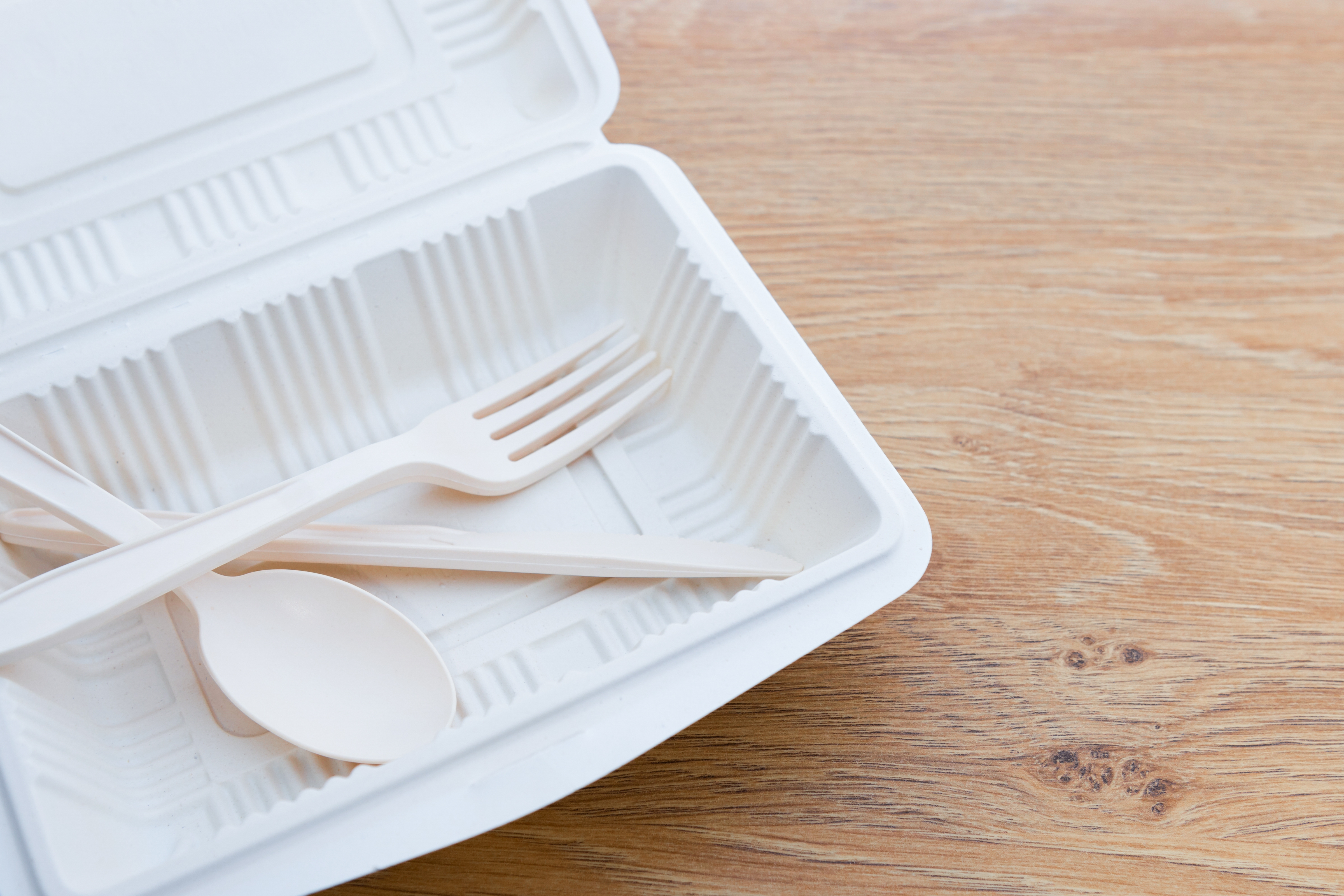 Une cuillère et une fourchette placées dans un contenant biodégradable d’aliments à emporter blanc placé sur une table en bois.