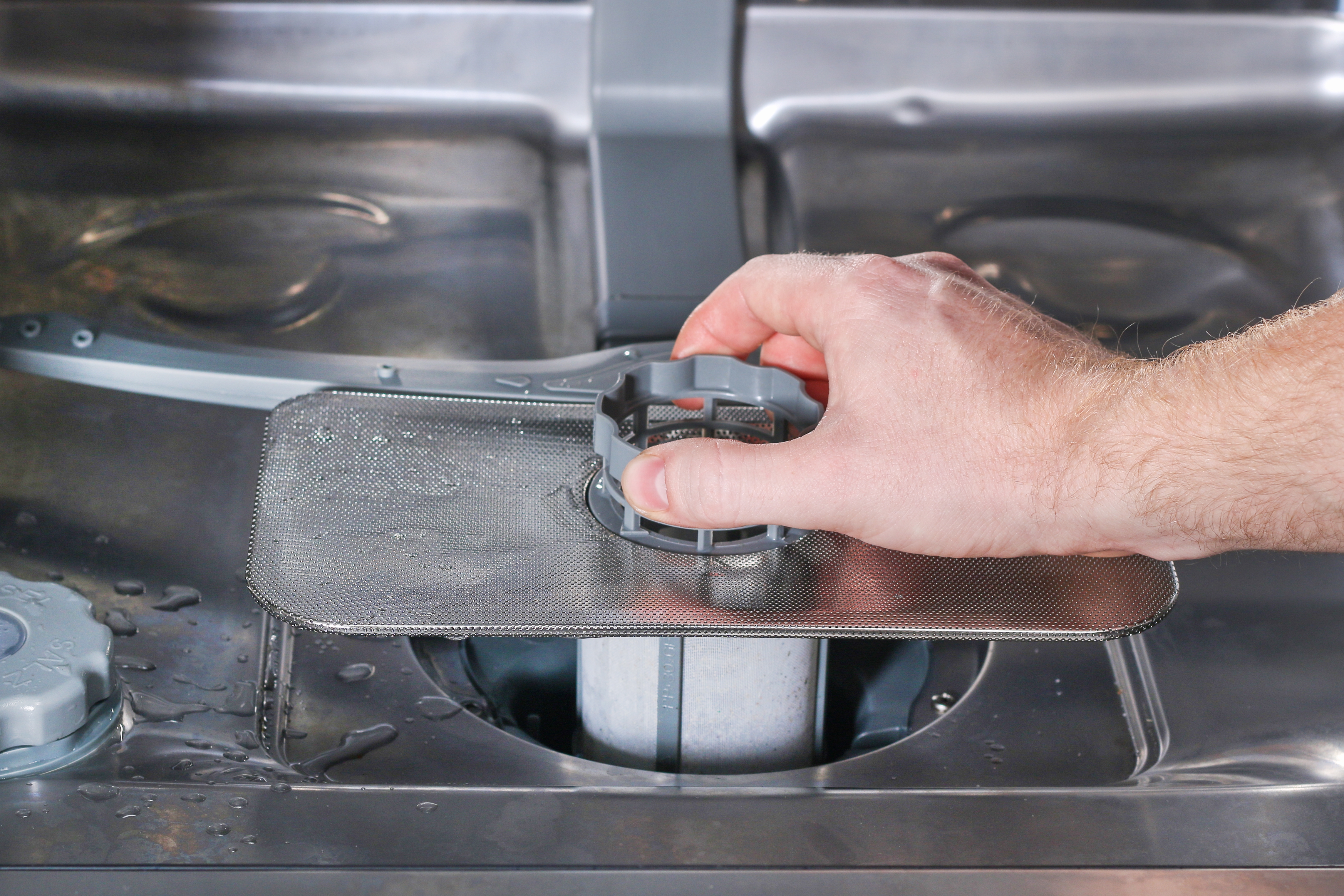 A hand reinserting a dishwasher filter into the base of the machine.