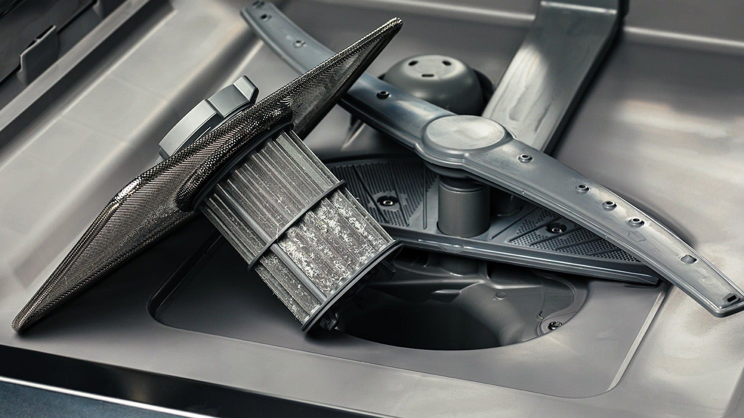 The bottom of a dishwasher with the filter removed and resting on its side.