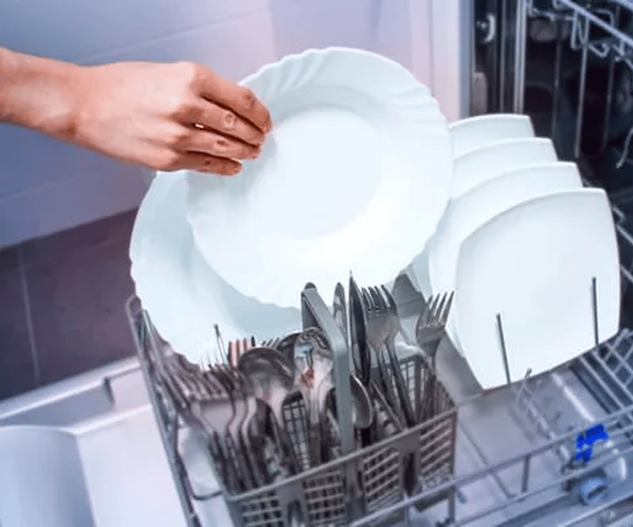 A hand takes out a clean, white plate from a dishwasher that is filled with neatly arranged plates and utensils.
