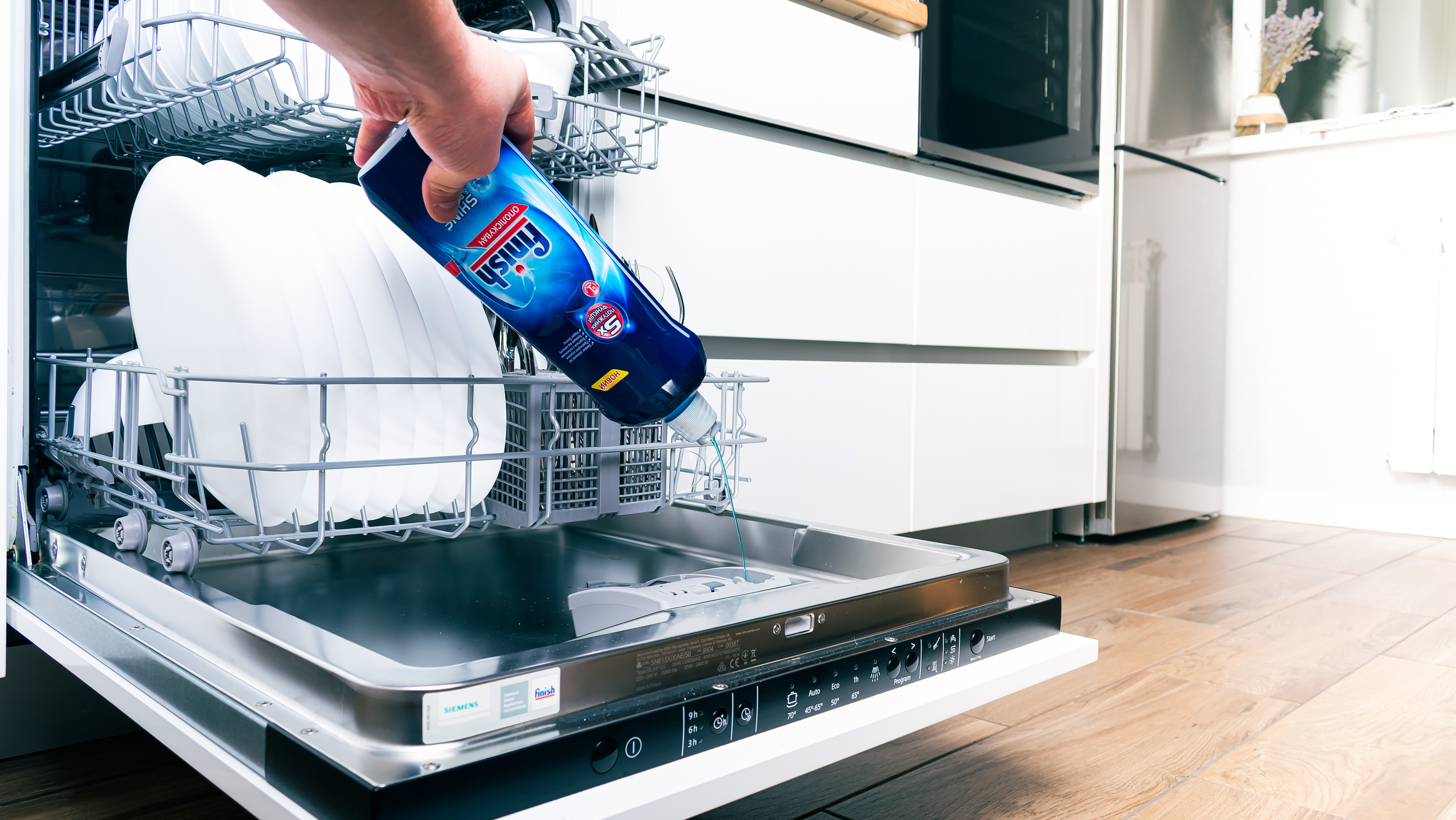 Pouring Finish Rinse Aid into a dishwasher to prevent cloudy glasses and hard water stains.
