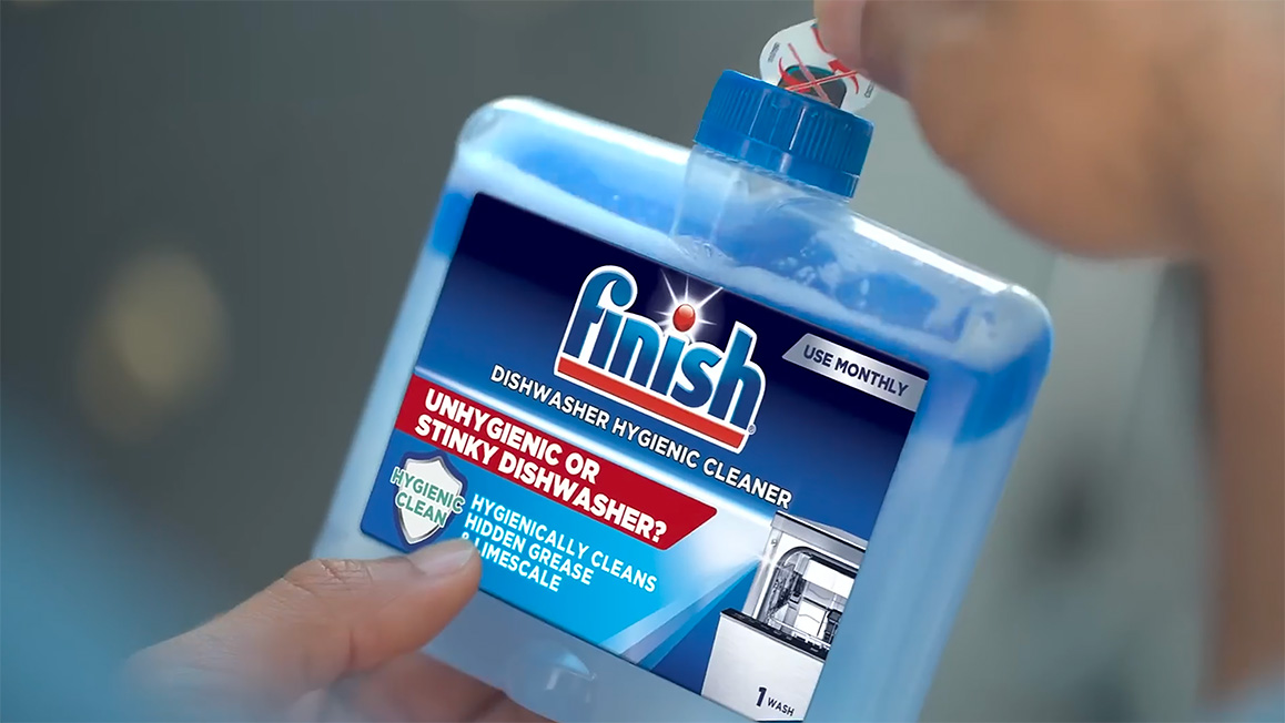 A woman’s hands hold a blue Finish Dishwasher Cleaner bottle and removes a sticker from the opening.