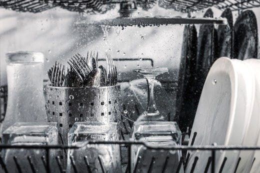 A running dishwasher filled with dishes, glasses, and utensils.