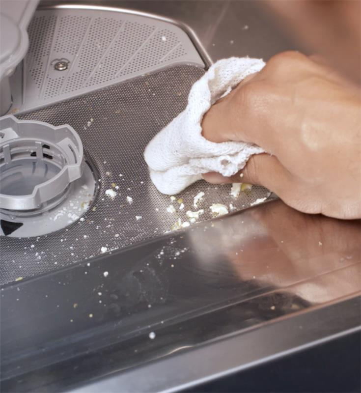 A woman’s hand scrubs the inside of a dishwasher with soap and a white cloth.