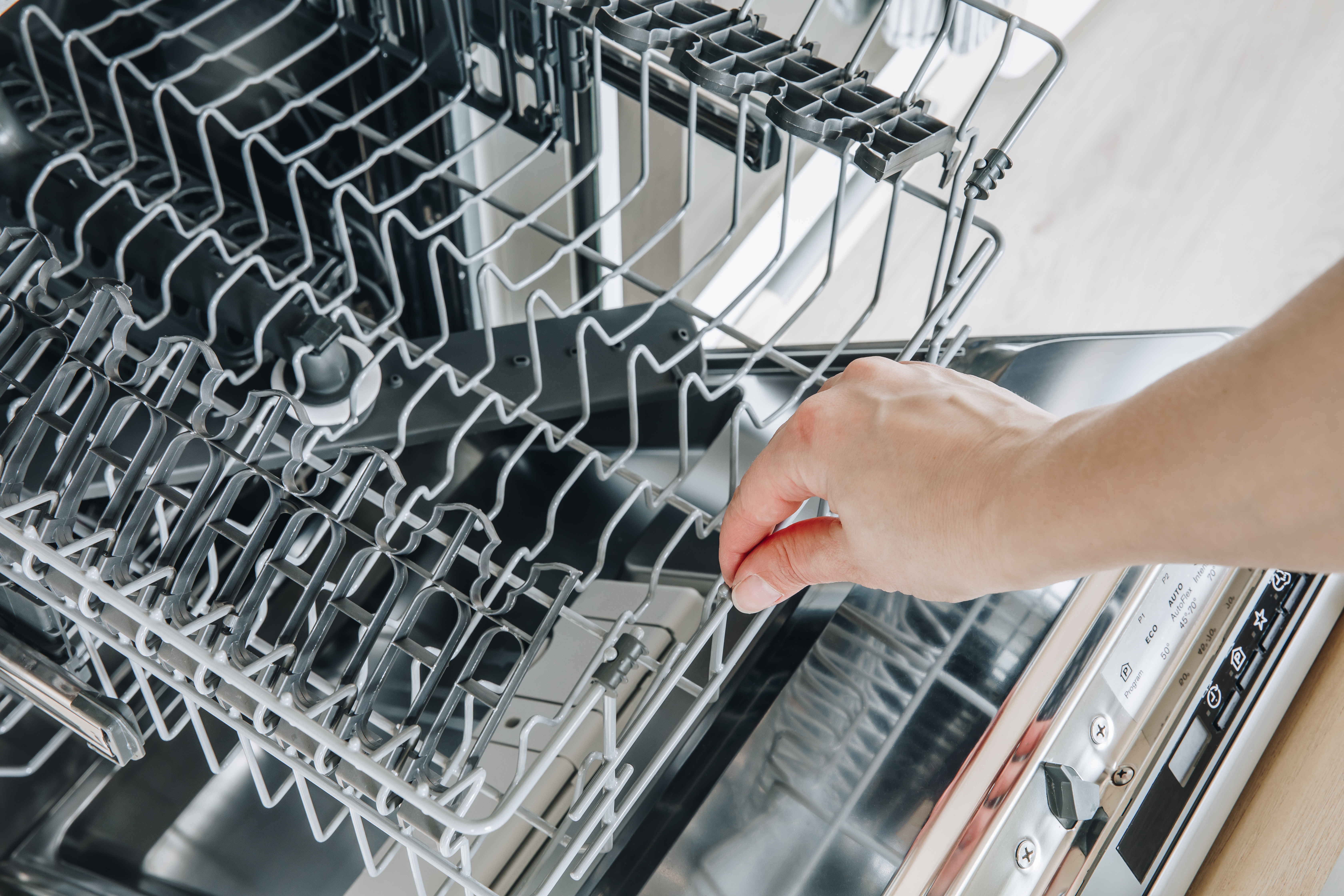 A hand sliding out the bottom rack of a dishwasher.