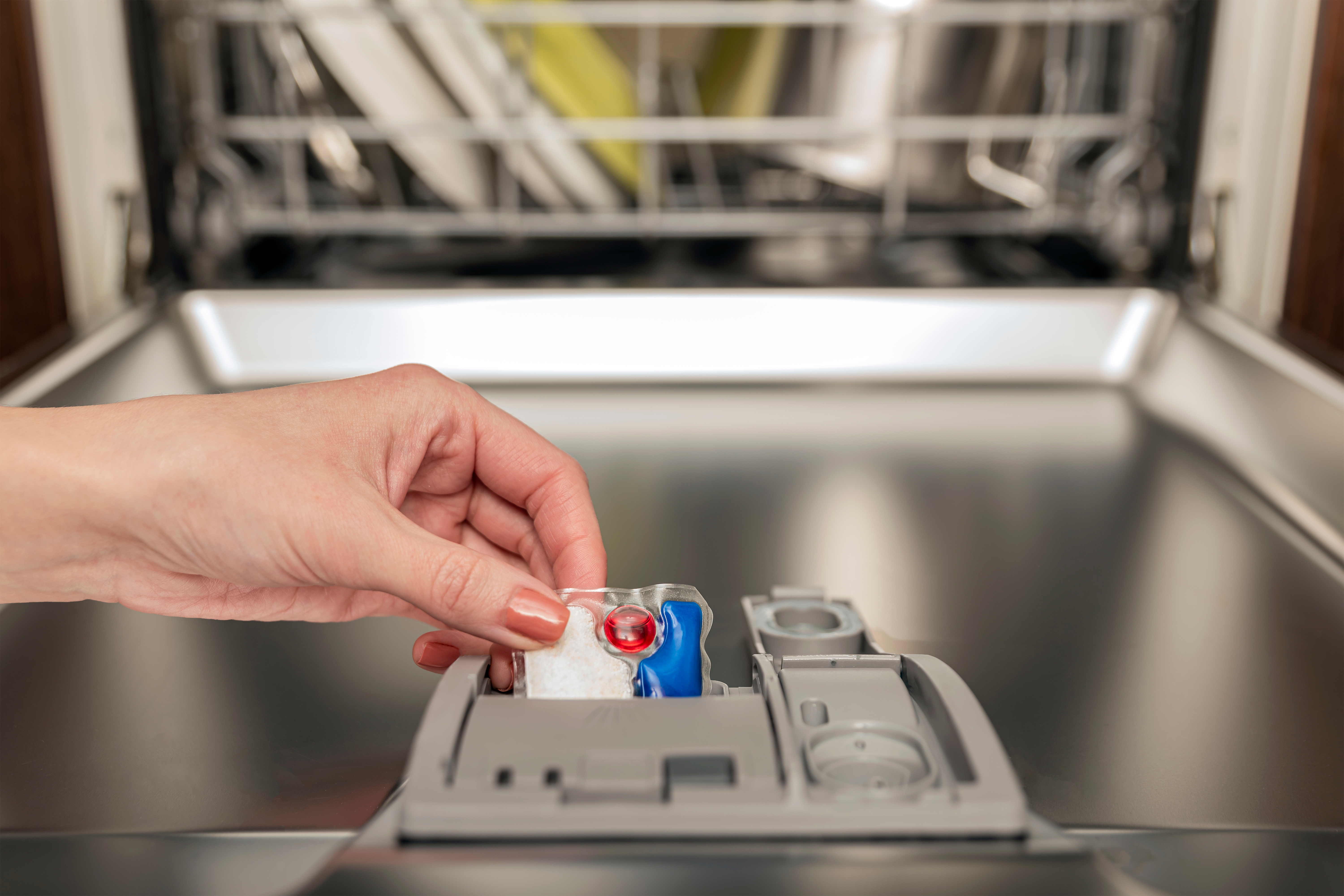 Une main insère une pastille dans le compartiment du distributeur de détergent d’un lave-vaisselle.